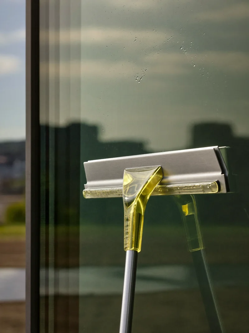 Abzieher gleitet über eine große Fensterscheibe mit Wassertropfen